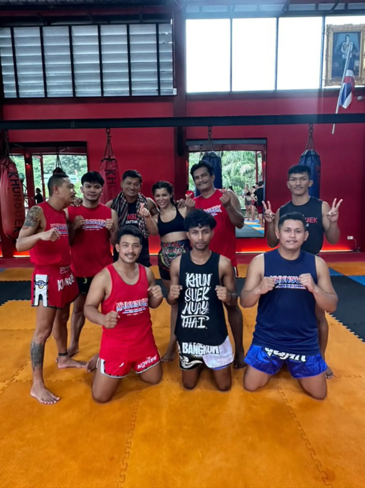 Group photo in the Muay Thai gym: Sarah surrounded by her coaches, with punching bags and tatami mats in the background