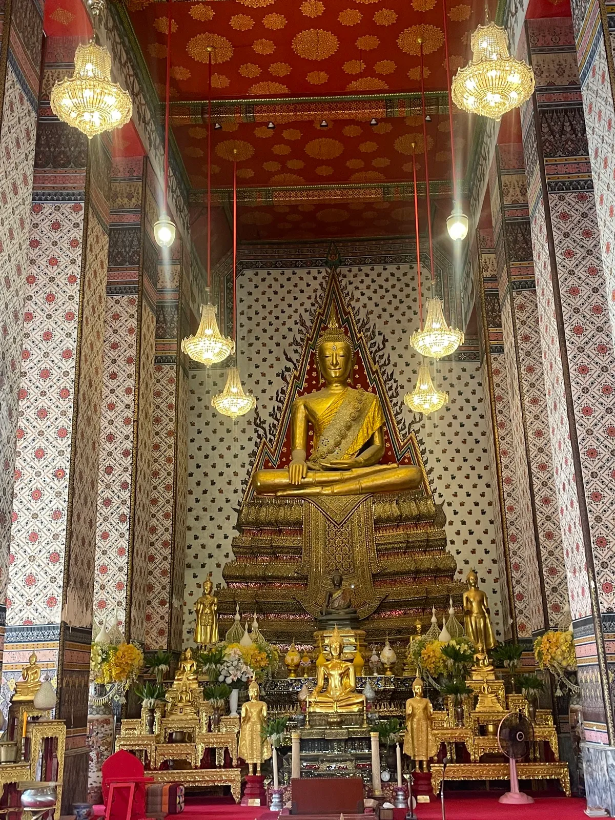 The interior of a temple: a golden Buddha beneath the chandeliers, columns painted with patterns