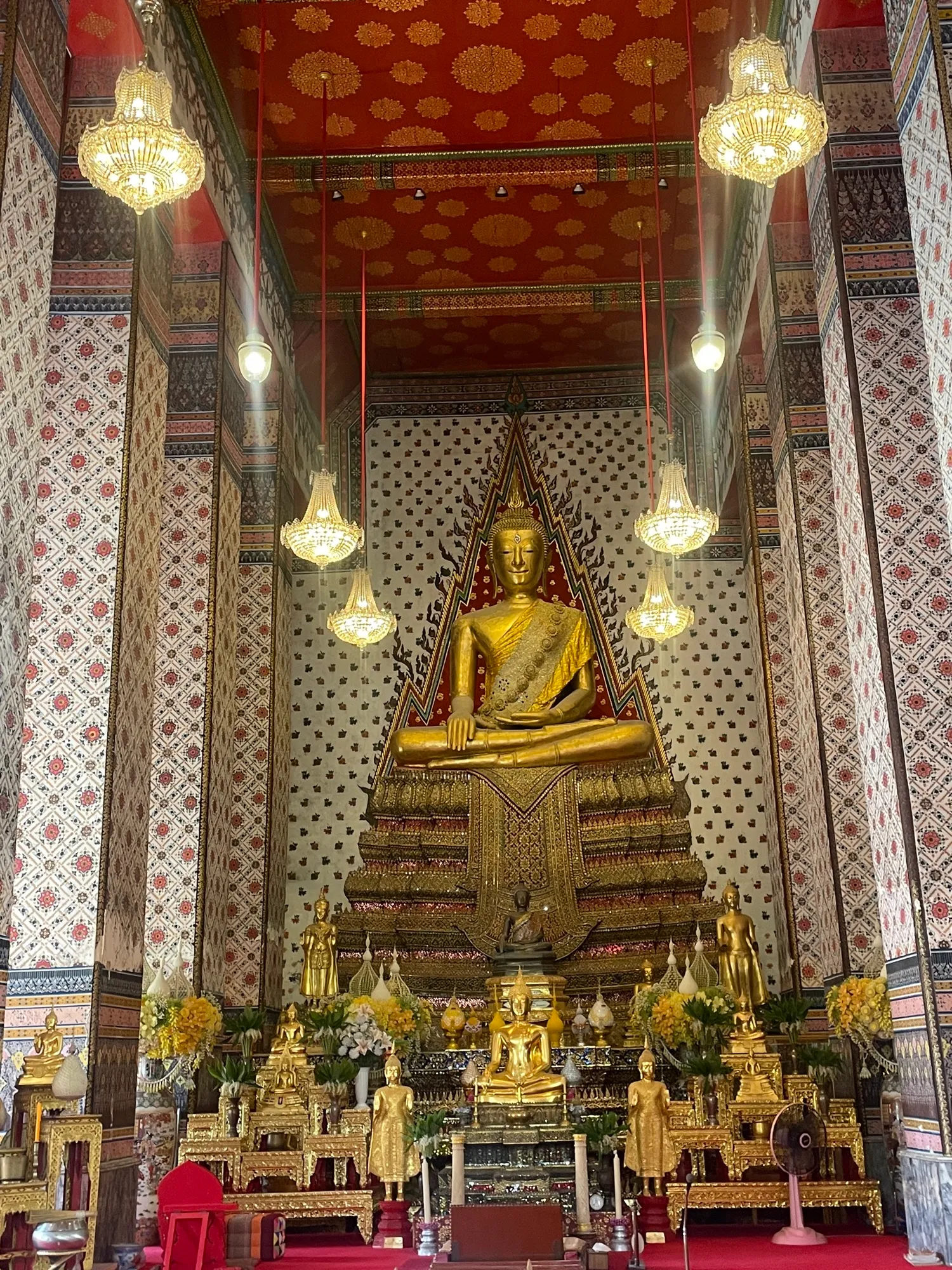 The interior of a temple: a golden Buddha beneath the chandeliers, columns painted with patterns